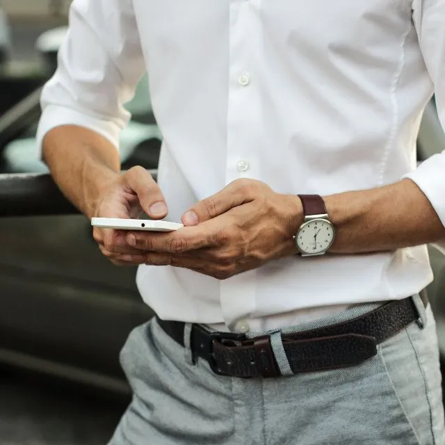A young man books on his phone, leaning against a car